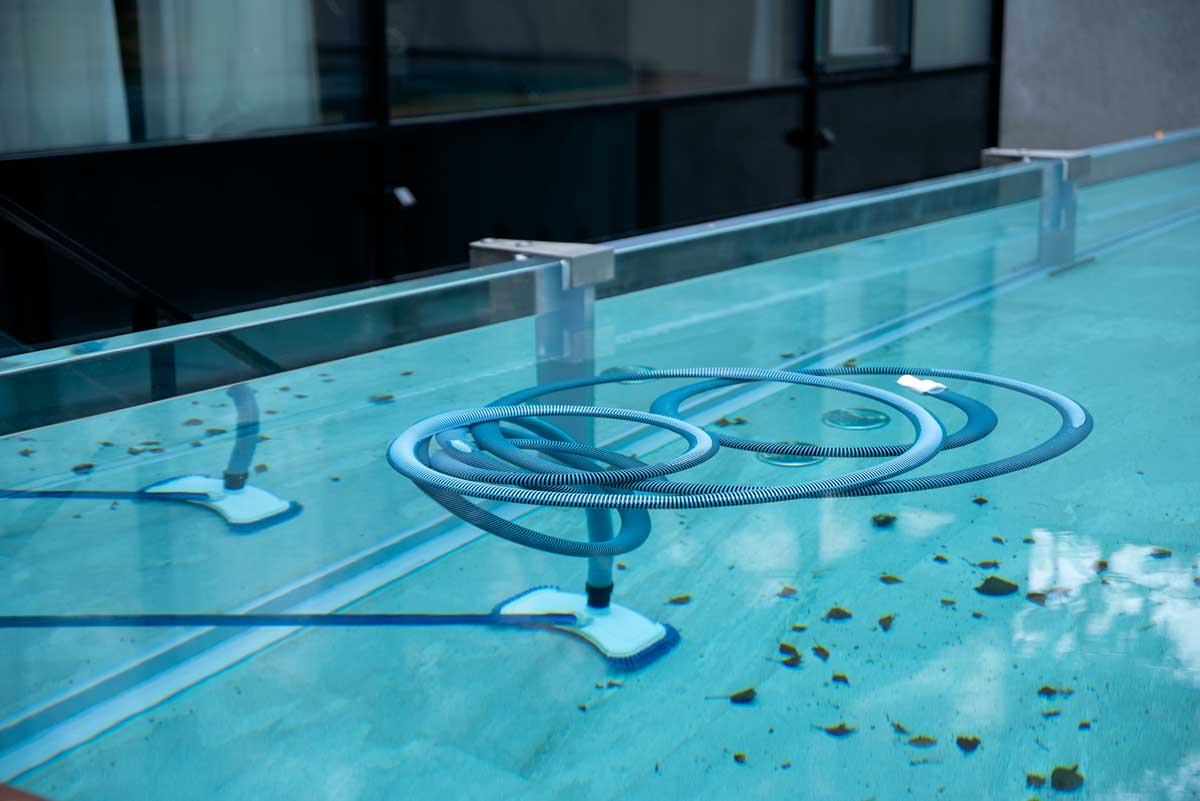Cleaning broom immersed in outdoor pool water, for cleaning the bottom and walls, pool full of leaves and other signs of neglect - dirt