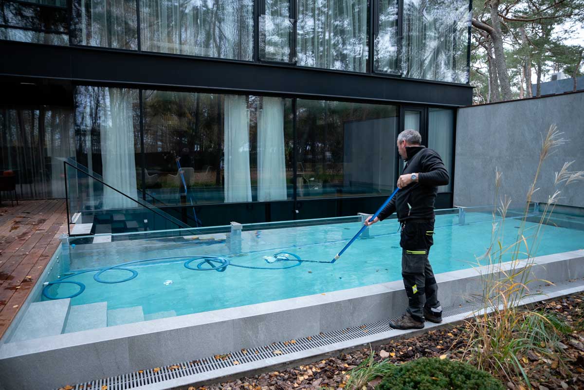 Outdoor swimming pool with cloudy and dirty water, brown spots and dirt visible on the surface, a person standing next to the pool