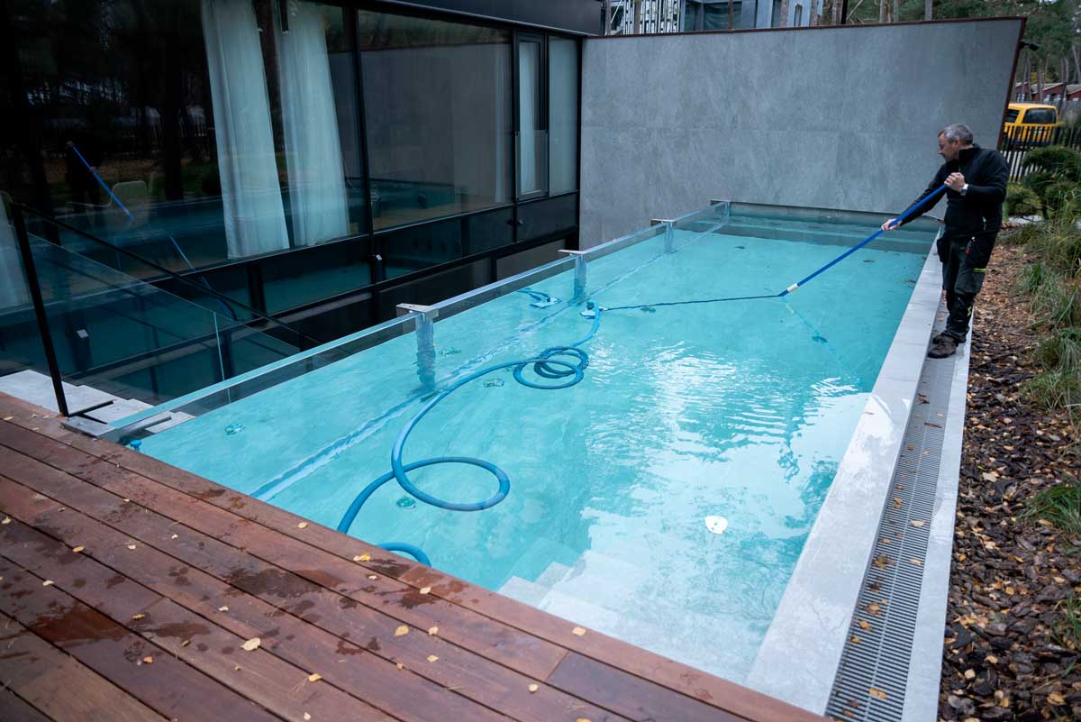 A swimming pool with light green and cloudy water, the surface covered with a layer of algae, a situation captured where there is a person cleaning the pool.