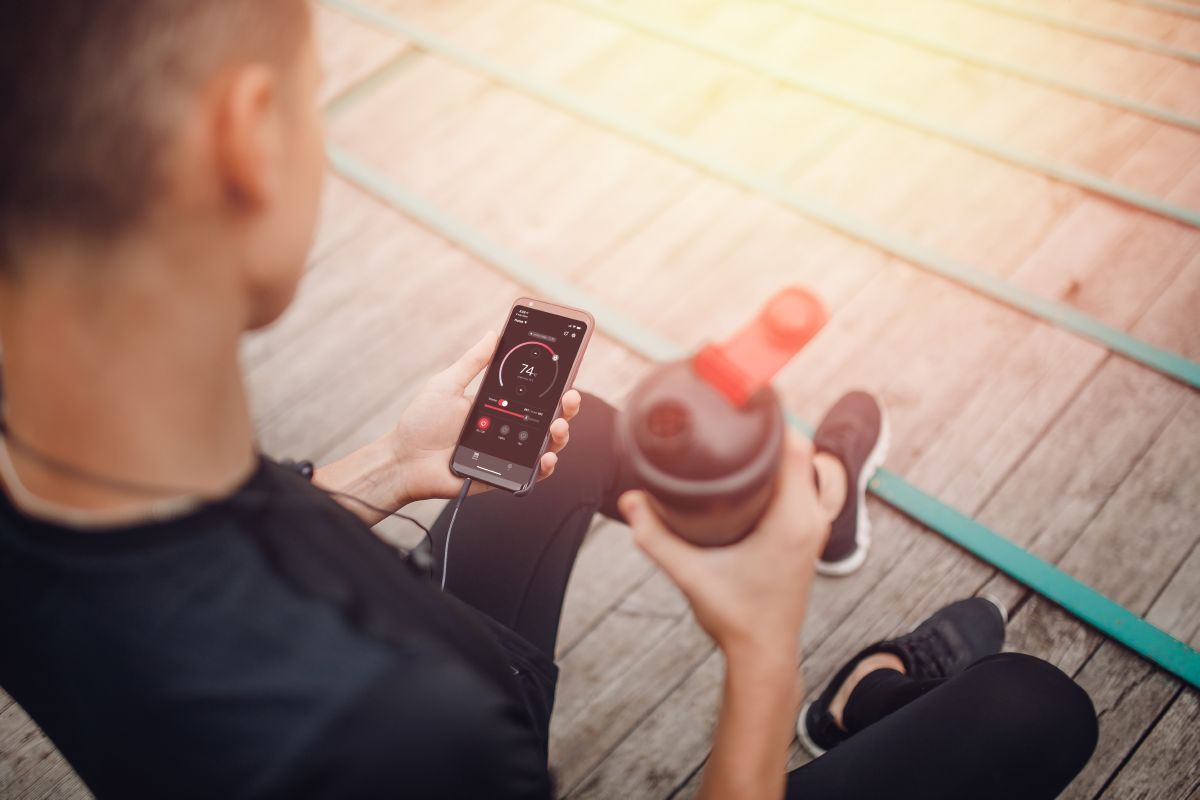 sportininkas rankose laiko gertuvę ir telefoną