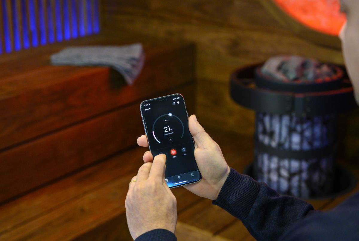 žmogus valdo pirties įrangą telefono programėlėje „MyHarvia“ 