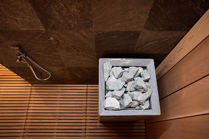 Top view of a sauna stove with light gray stones, wooden grates, and dark wall tiles.