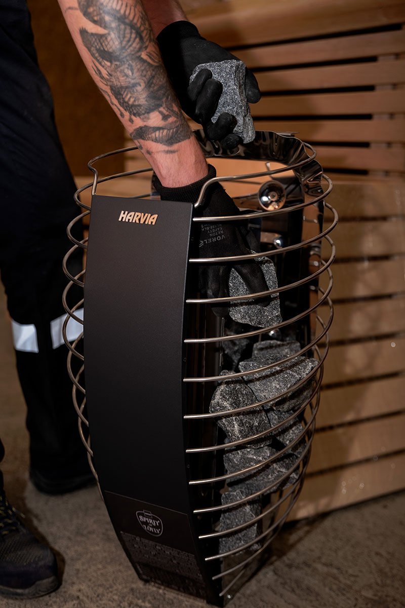 Close-up of the basket of a HARVIA electric stove: dark gray sauna stones are placed in black gloves.