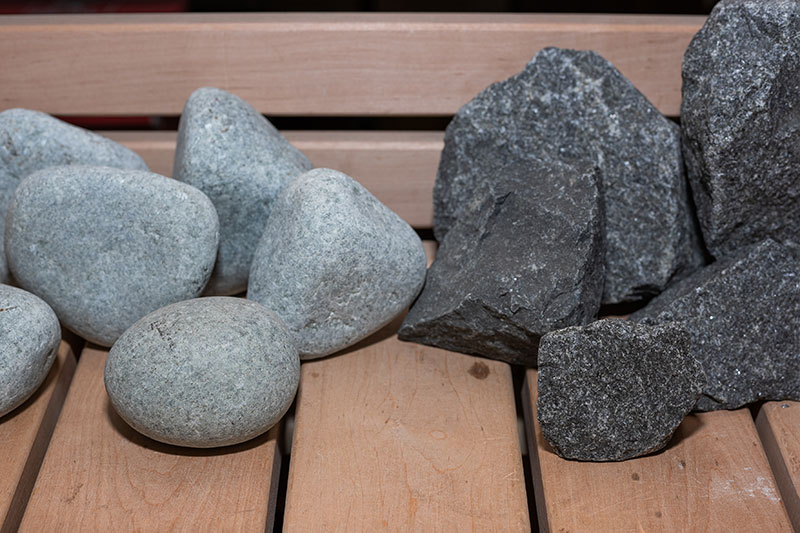 Comparison: rounded light-colored river stones and broken dark sauna stones placed on a wooden bench.