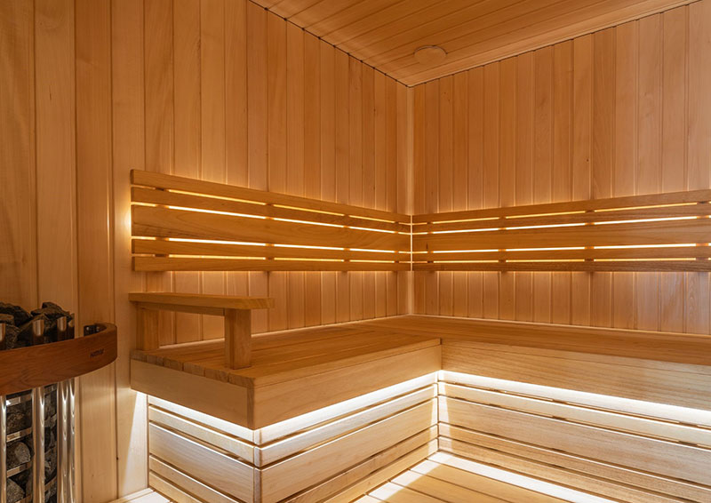 Moderni šviesaus medžio pirtis su kampiniais gultais ir paslėptu LED.