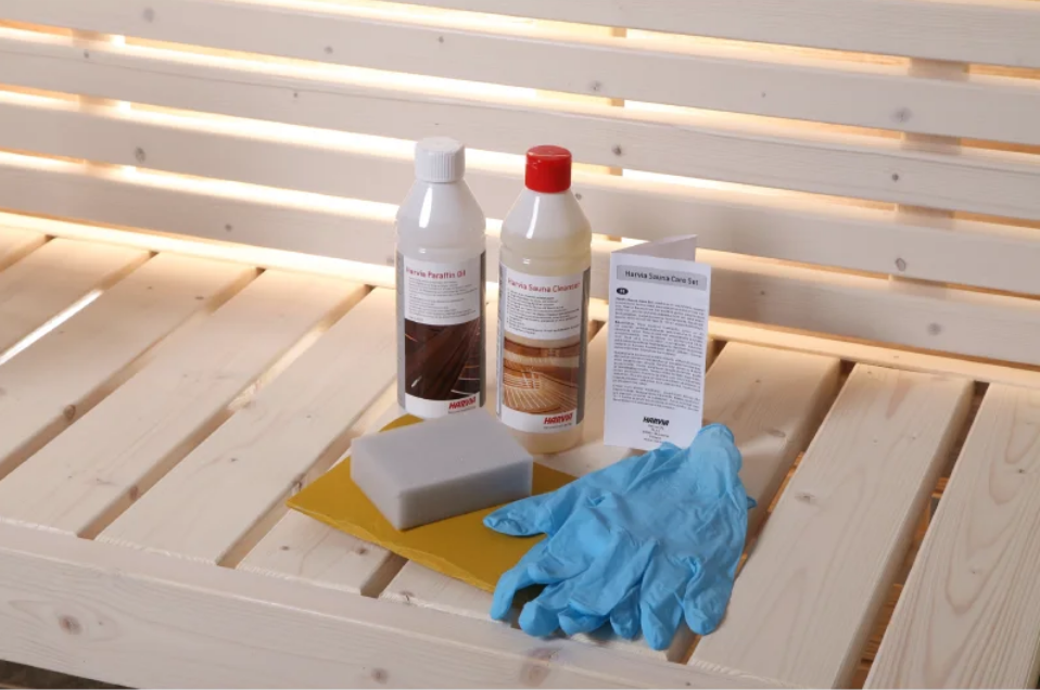 Sauna maintenance kit on a wooden bench board – cleaning products, oil, sponge, rubber gloves, and instructions.