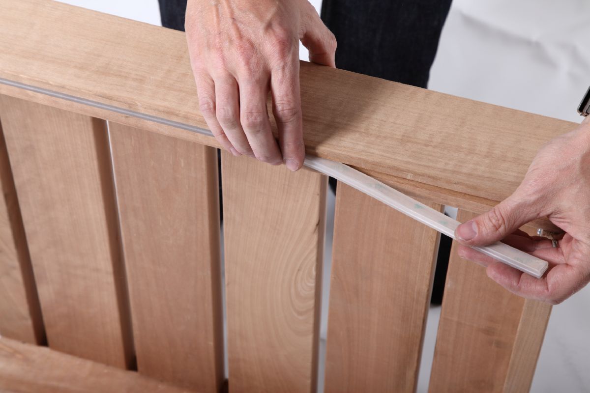 Human hands are installing a silicone strip on the edge of a wooden sauna wall.