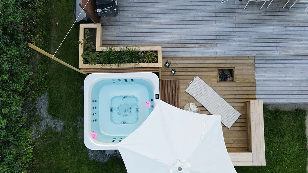Spa pool from above, located on a wooden terrace with a lounger, plants and a parasol, overlooking the surrounding courtyard